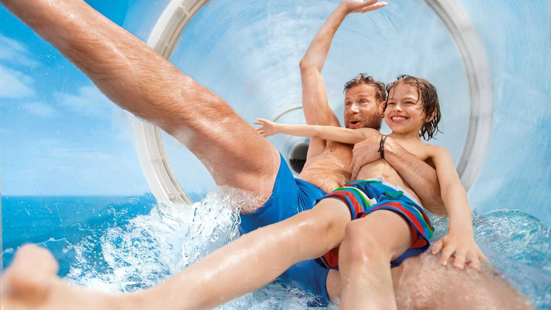 Vater und Sohn genießen eine Wasserrutsche auf einer AIDA Kreuzfahrt, lachend und voller Spaß
