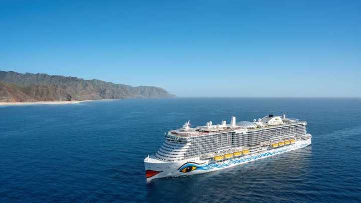 Kreuzfahrtschiff von AIDA Cruises vor einer malerischen Küstenlandschaft Kreuzfahrtschiff von AIDA Cruises auf dem Meer mit einer bergigen Küste im Hintergrund