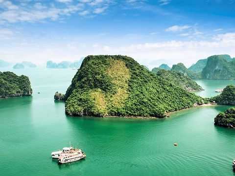Karstfelsen ragen aus dem türkisgrünen Wasser der Halong-Bucht mit traditionellen Booten.