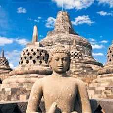 Stein-Buddhastatue vor den historischen Stupas des Borobudur-Tempels in Indonesien bei blauem Himmel