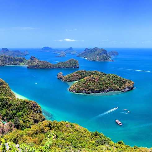 Luftaufnahme tropischer Inseln in türkisblauem Meer mit Booten und üppiger Vegetation unter klarem Himmel.
