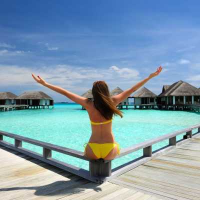 Frau im gelben Bikini genießt das Paradies auf einem Steg vor Malediven Wasserbungalows