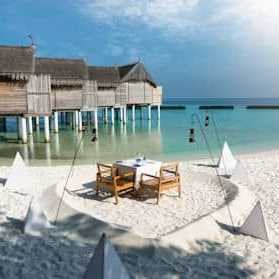Romantisch gedeckter Tisch im Sand direkt am Meer mit Blick auf Wasserbungalows auf den Malediven