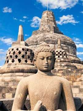 Stein-Buddhastatue vor den historischen Stupas des Borobudur-Tempels in Indonesien bei blauem Himmel