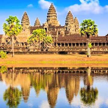 Historischer Tempel Angkor Wat in Kambodscha mit Palmen im Vordergrund und dramatischem Himmel im Hintergrund.