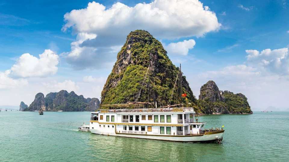 Weißes Ausflugsschiff vor steil aufragenden Kalksteinfelsen in der Halong-Bucht - Vietnam Rundreise und baden.