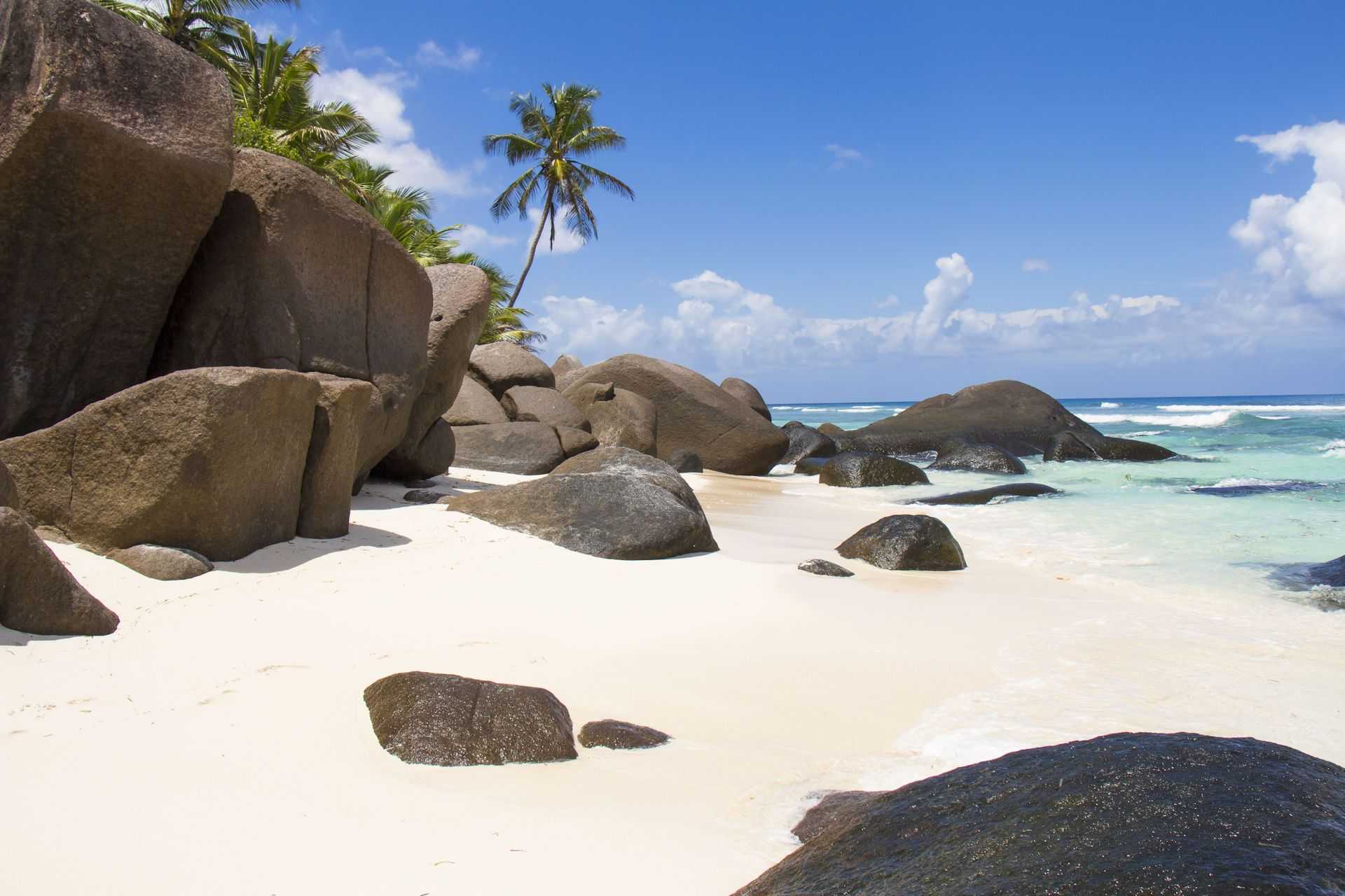 Granitfelsen am weißen Sandstrand von La Digue, Seychellen mit Palmen und blauem Himmel