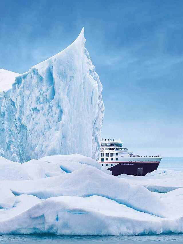 Arktis-Expedition buchen – Entdecken Sie die unberührte Natur mit Hapag-Lloyd Cruises Expeditionsschiff Hanseatic Nature von Hapag-Lloyd Cruises neben einem riesigen Eisberg in der Arktis