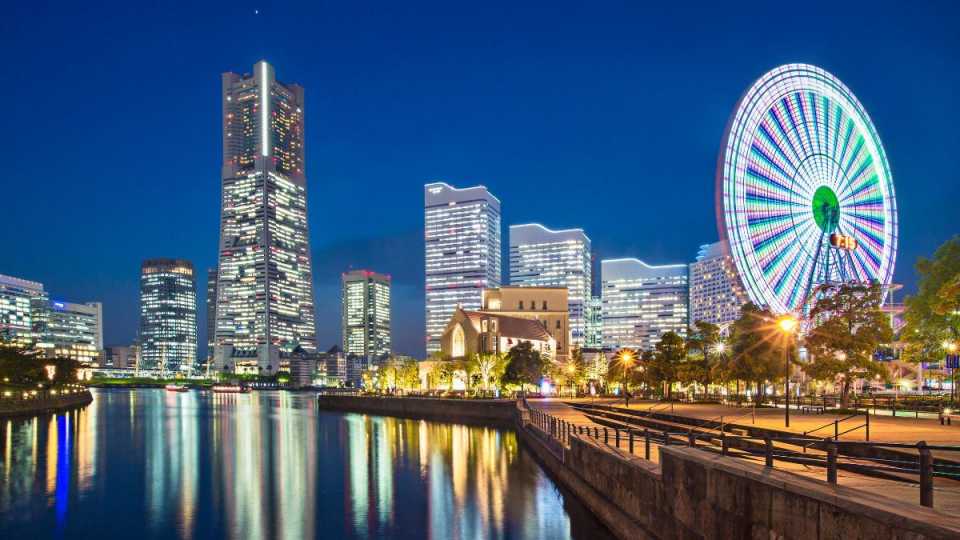 Weltreise buchen - Städte bei Nacht – Faszinierende Skylines und kulturelle Highlights entdecken Beleuchtete Skyline einer Stadt bei Nacht mit Hochhäusern und einem großen Riesenrad, das sich im Wasser spiegelt