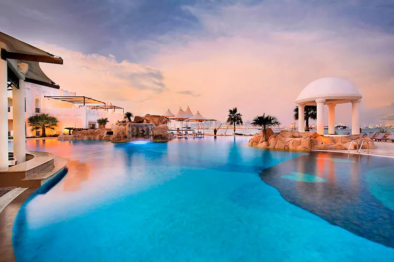Luxus-Kombireise Doha: Exklusiver Infinity-Pool im Sharq Village & Spa mit traditioneller katarischer Architektur bei Sonnenuntergang – Auftakt der JUREBU Signature Journey.