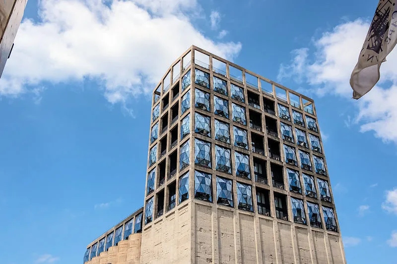 Luxus-Kombireise Kapstadt: Die markante Außenansicht des The Silo Hotels mit seinen ikonischen Glasfenstern vor blauem Himmel – architektonisches Highlight von JUREBU.