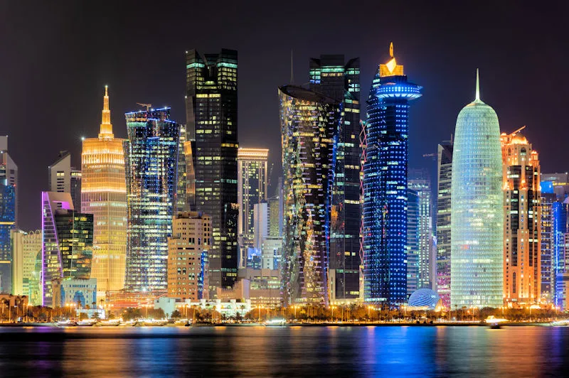 Luxusreise Katar Doha Skyline bei Nacht mit beleuchteten Wolkenkratzern der West Bay am Persischen Golf