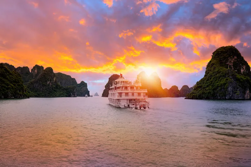 Luxus Reiseziel Vietnam - Segeln durch die Legende: Die mystische Halong-Bucht im warmen, goldenen Glanz der untergehenden Sonne.